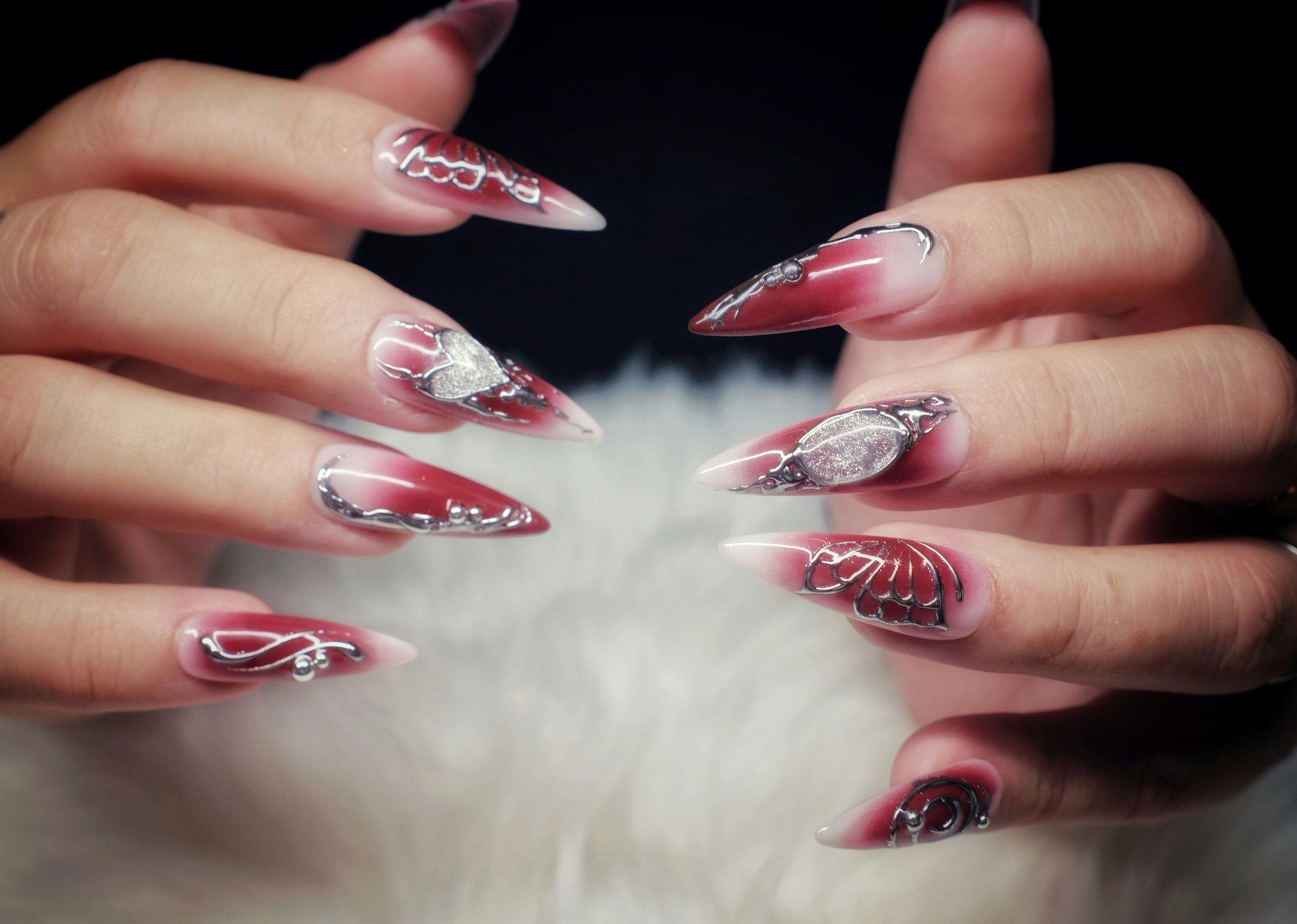 Long stiletto nails in a rosewood-to-white ombre with sculpted silver linework