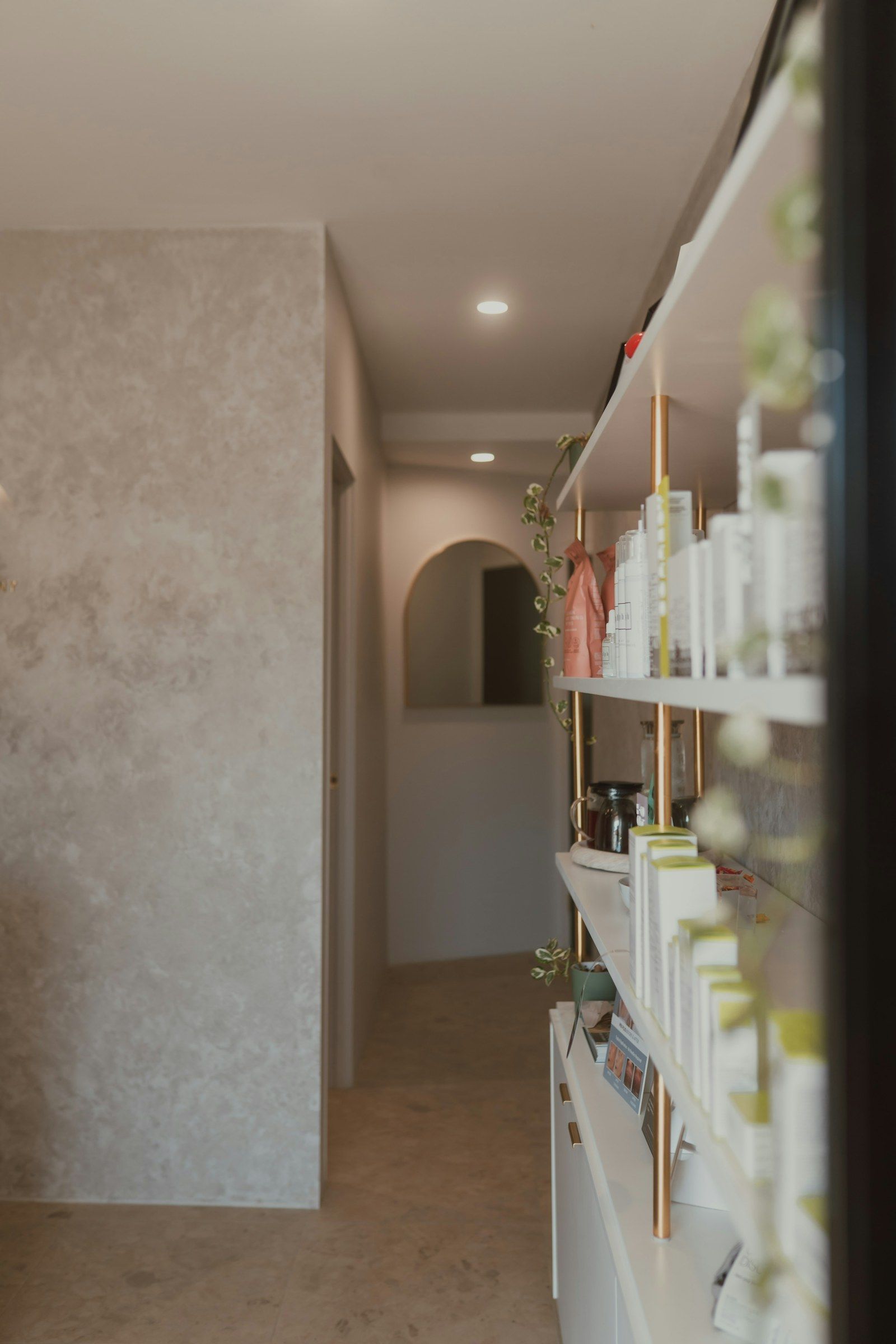 A softly lit hallway with an arched doorway and shelves of skin care