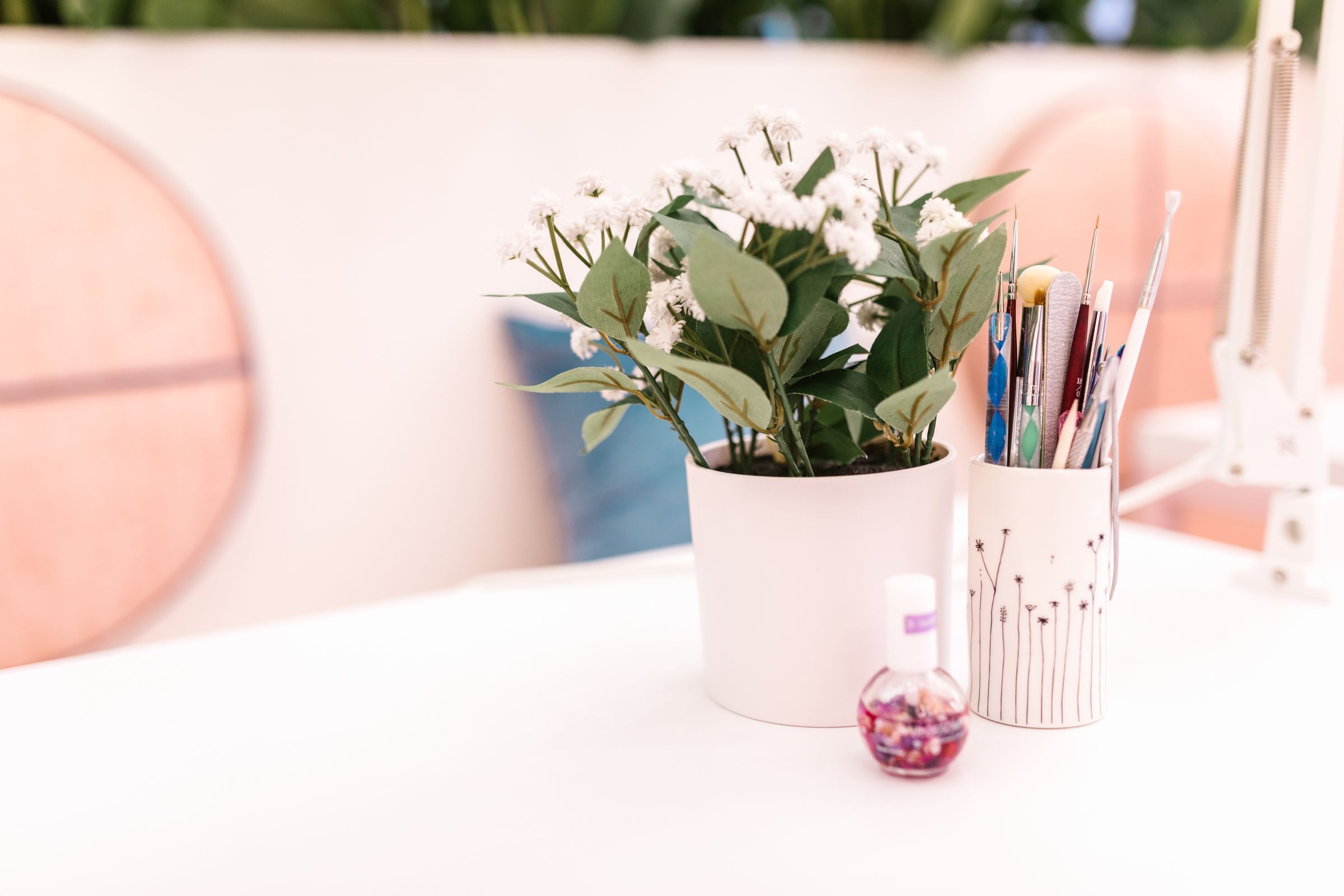 A white counter with fresh flowers, a pot of nail-art brushes and cuticle oil