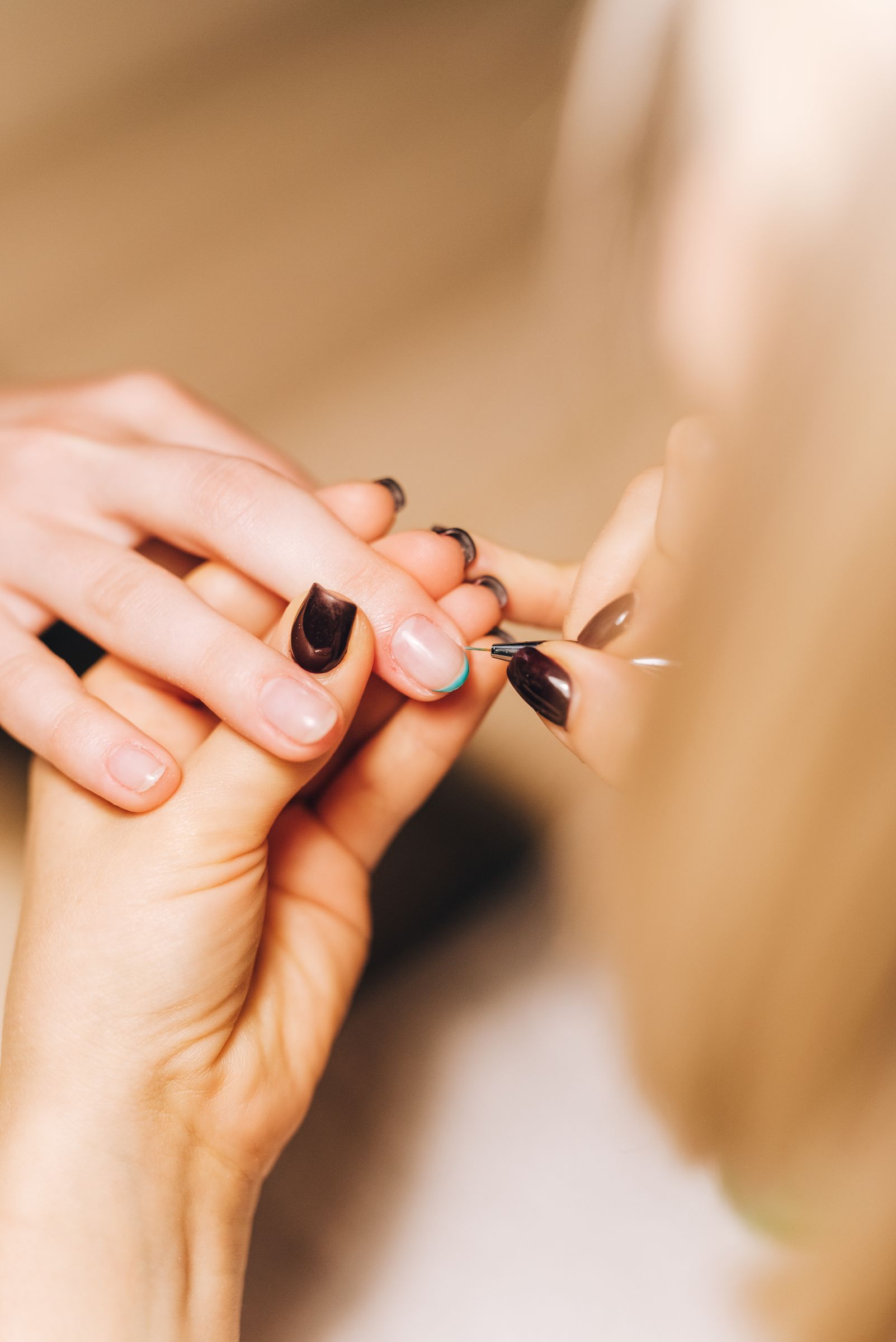 An artist painting fine detail onto a client’s dark gel nail